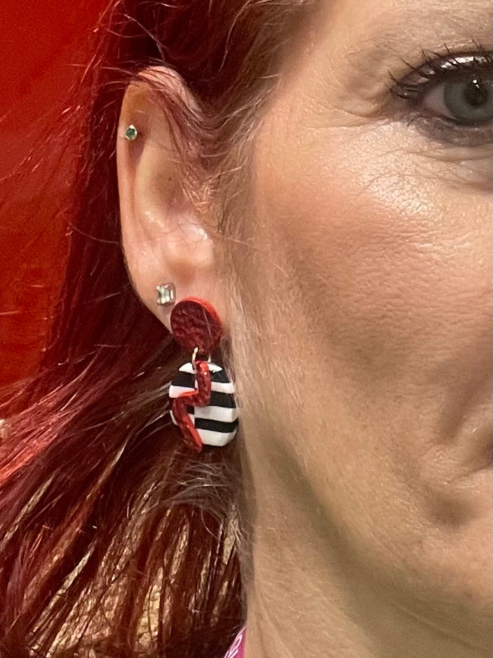 Spice up your look with these funky and vibrant earrings! Featuring a striking red lightning bolt on a bold black and white backdrop, these handmade beauties are sure to make a statement. Crafted from red clay and accented with shiny red foil, these earrings have a unique hammered texture.