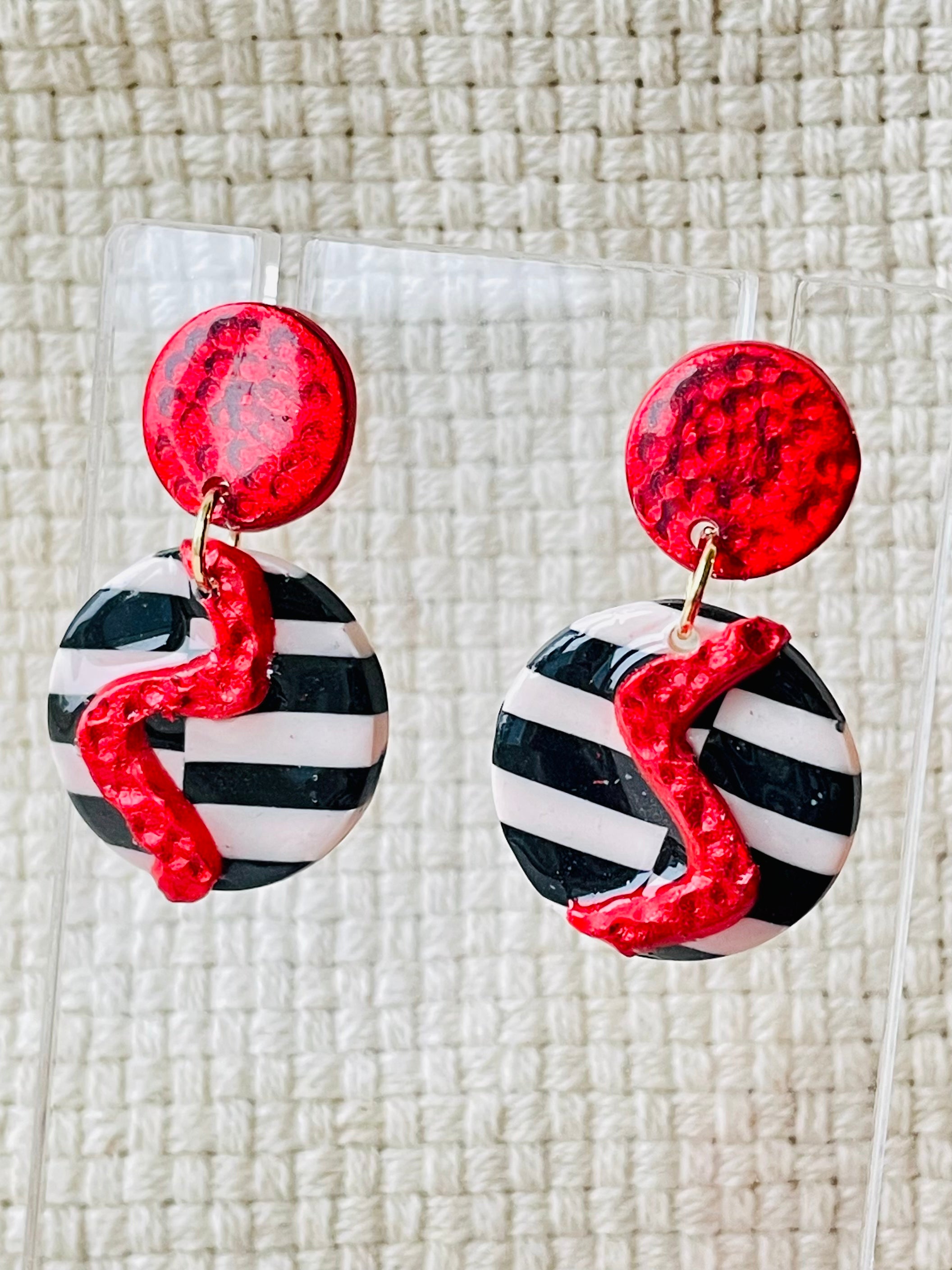 Spice up your look with these funky and vibrant earrings! Featuring a striking red lightning bolt on a bold black and white backdrop, these handmade beauties are sure to make a statement. Crafted from red clay and accented with shiny red foil, these earrings have a unique hammered texture.